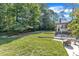 View of a lush backyard with green grass, mature trees, and a patio area with outdoor seating at 1920 Hillock Dr, Raleigh, NC 27612