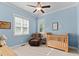 Light blue bedroom with a wooden crib, recliner chair, and natural light streaming through the window at 1412 Wakefield Farm Rd, Zebulon, NC 27597