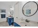 Bright bathroom featuring blue vanity, updated fixtures, a large round mirror, and white walls at 14393 Nc Hwy 96 N, Zebulon, NC 27597