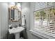 Charming powder room featuring a pedestal sink, decorative mirror, and natural light from the window at 1702 Mcrae Pl, Hillsborough, NC 27278