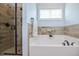 Bright bathroom featuring a walk-in shower, a soaking tub with decorative tile surround, and a large window at 18 Heathgreen Dr, Clayton, NC 27527