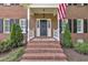 Inviting front entry with brick steps, white columns, and an American flag, surrounded by manicured greenery at 418 Old Scarborough Ln, Garner, NC 27529