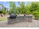 Outdoor kitchen area with brick surround, stone countertop, built-in grill, and a beautifully landscaped background at 623 Westfall Way, Chapel Hill, NC 27517