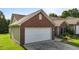 Side view of the brick home featuring an attached garage with a white door and concrete driveway at 3027 Maple Ave # U1, Burlington, NC 27215