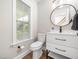 Well-lit powder room with a white vanity, a round mirror, and a toilet near a window at 4502 Joe Cotton Dr, Knightdale, NC 27545