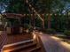 Charming backyard featuring an inviting outdoor dining area, surrounded by mature trees and soft, ambient lighting at 4716 Shadow Ridge Ct, Holly Springs, NC 27540