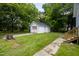View of the detached, single-car garage with white siding and black roof, surrounded by mature trees at 605 E Montgomery St, Henderson, NC 27536