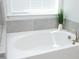 Bright white bathtub featuring a window, brushed nickel fixtures, and neutral-toned ceramic tiling at 609 Ramsours Mill Dr, Holly Springs, NC 27540