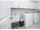 Functional laundry room with upper cabinets, utility sink, washer, and dryer on tiled flooring at 609 Ramsours Mill Dr, Holly Springs, NC 27540