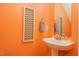 Cozy powder room with an orange accent wall, pedestal sink, and a decorative mirror at 109 Troyer Pl, Apex, NC 27502