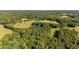 Wide aerial photo features a home surrounded by trees and vast fields, creating a serene and picturesque landscape at 1973 Elon Ossipee Rd, Elon, NC 27244