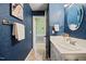 Stylish bathroom with blue wallpaper, gold fixtures, a white vanity, and ample lighting at 1973 Elon Ossipee Rd, Elon, NC 27244