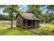 Rustic wooden shed featuring a weathered exterior, porch and mature shade trees at 7404 Halifax Rd, Youngsville, NC 27596
