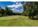 View of a lush green golf course from the property, surrounded by mature trees on a partly cloudy day at 121 Walter Hagen Dr, Mebane, NC 27302