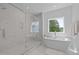 Bright bathroom with a marble walk-in shower and soaking tub beneath a window with wooded views at 1338 The Parks Dr, Pittsboro, NC 27312