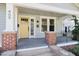 Inviting front porch featuring brick columns, grey painted floors and a bright yellow front door at 409 N Hyde Park Ave, Durham, NC 27703