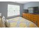 Bright bedroom featuring a large window, yellow patterned bedding, and a wooden dresser with two TVs at 5113 Lady Of The Lake Dr, Raleigh, NC 27612