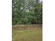 A backyard featuring a stone retaining wall and black metal fence bordering a lush wooded area, blending privacy with natural scenery at 2008 Van Hook Ln, Apex, NC 27502
