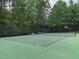 Community tennis court with green surface, basketball hoop, bench, and surrounding woods at 1000 Clovelly Ct, Raleigh, NC 27614