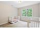 Bedroom with two cribs, carpeted floor, and a window offering natural light and backyard view at 14 Gloucester Ct, Durham, NC 27713