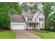 Traditional two-story home with attached garage, front porch, and manicured lawn surrounded by mature trees at 1208 Mossy Glade Cir, Apex, NC 27502