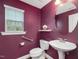 This powder room features a pedestal sink, round mirror, burgundy walls and a window for natural light at 136 Shadow Hawk Dr, Durham, NC 27713