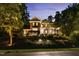 A beautiful brick home with exterior lighting highlighting a well-manicured front yard at dusk at 4021 Chaumont Dr, Apex, NC 27539