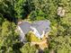 Aerial view showcasing the home's layout, roof, yard, and landscaping amidst a lush green forest setting at 676 Whitehurst, Pittsboro, NC 27312