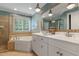 Bathroom showcasing double vanity, ornate mirror, soaking tub by the window, and shower with glass door at 200 Cobblepoint Way, Holly Springs, NC 27540