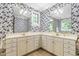 A bathroom with a long white vanity with dual sinks, gold hardware and mirrors, and wallpaper with a floral design at 228 Birch Creek Dr, Fuquay Varina, NC 27526