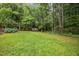 Lush backyard featuring manicured lawn, flower beds, and a shed surrounded by a forest at 7520 Milestone Ct, Raleigh, NC 27615