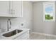 Bright laundry room features white cabinets, a stainless steel sink, and a window letting in natural light at 7719 Barefoot Rd, Fuquay Varina, NC 27526