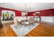 Elegant dining room with red accent wall, hardwood floors, and seating for six, complemented by stylish decor and abundant light at 5200 Pulley Town Rd, Zebulon, NC 27597