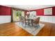 Formal dining room with elegant red walls, hardwood floors, large windows, and seating for six, creating a refined space at 5200 Pulley Town Rd, Zebulon, NC 27597