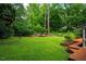 Lush green backyard featuring a manicured lawn, garden beds, and a charming deck at 69 Margaret Pl, Chapel Hill, NC 27516