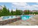 Inviting backyard pool and spa area surrounded by lush greenery and a stone patio at 120 Hazel Alder Ct, Holly Springs, NC 27540