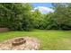 An outdoor stone fire pit surrounded by lush grass and mature trees creates a serene backyard setting at 1217 Heritage Greens Dr, Wake Forest, NC 27587