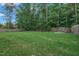 Large, fenced backyard with lush green grass, mature trees, and a fire pit with seating area at 2018 Morehead Hill Ct, Durham, NC 27703