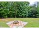 Large backyard with a cozy fire pit and seating area, surrounded by mature trees at 67 Marshlane Way, Clayton, NC 27527