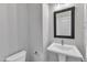 A well-lit half bathroom with a white pedestal sink, black framed mirror, and neutral wall color at 816 Lilyquist Way, Wake Forest, NC 27587