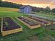 View of raised garden beds with a barn in the background under a colorful sky at 8365 Aaron Creek Church Rd, Oxford, NC 27565