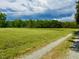 Expansive grassy land with a treeline in the background and a gravel path at 8365 Aaron Creek Church Rd, Oxford, NC 27565