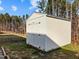 A small storage shed with double doors sits in a grassy backyard with a forest background on a sunny day at 274 E Boulder Road Rd, Henderson, NC 27537