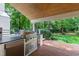 Covered outdoor kitchen with a built-in grill, stainless steel cabinets, and brick flooring, ideal for backyard gatherings at 1301 King Cross Ct, Raleigh, NC 27614