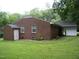 Rear exterior view of brick home with manicured lawn, partial carport, and additional storage shed at 1809 S Garnett Ext, Henderson, NC 27536