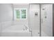 Modern bathroom featuring a soaking tub and separate glass-enclosed shower, white tile, and natural light at 2083 Amalfi Pl, Apex, NC 27502