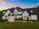 A grand two-story home featuring a manicured lawn, striking white brick, and black trim against a colorful sunset sky at 2220 Inwood Landing Ct, Raleigh, NC 27603