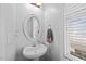 Charming half-bathroom featuring a pedestal sink, oval mirror, and natural light from the window at 224 Swann Trl, Clayton, NC 27527