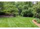 Expansive green backyard featuring lush lawn, privacy trees, and colorful flower beds at 3307 Devon Rd, Durham, NC 27707