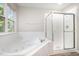 Bright bathroom featuring a soaking tub, separate shower, and a window overlooking a green outdoor view at 1527 Haywards Heath Ln, Apex, NC 27502